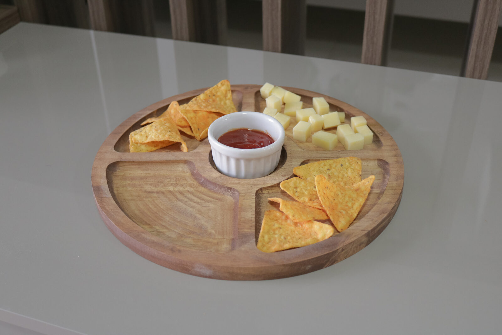 Tábua redonda de madeira com ramekim central de porcelana, nachos e queijos servidos