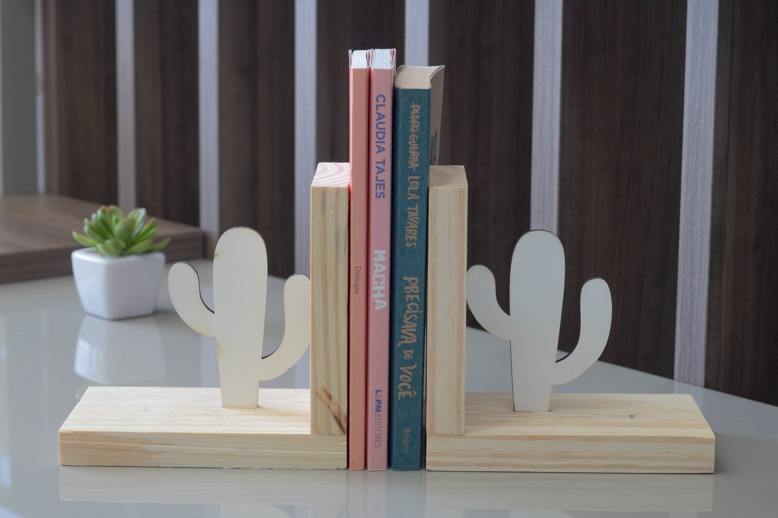 Par de aparadores de livros de madeira pinus com recorte de cactus segurando livros sobre mesa
